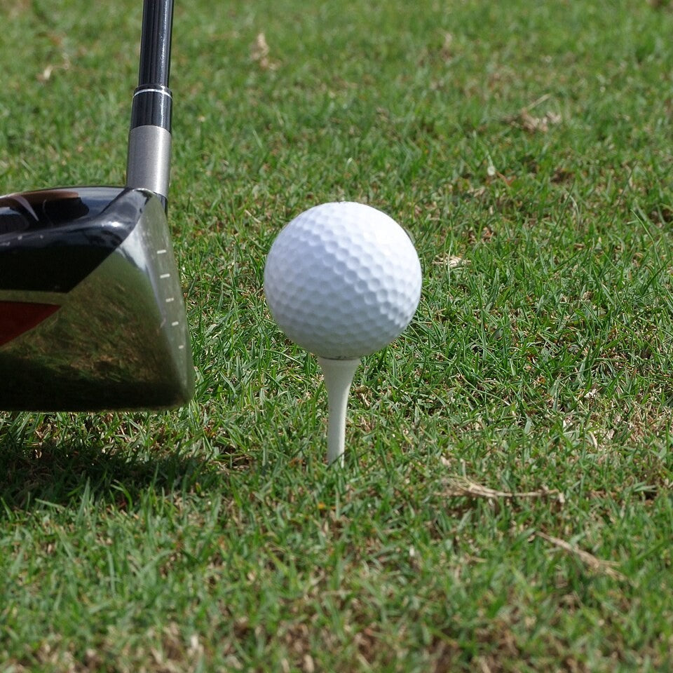 A golf ball on a tee beside a driver