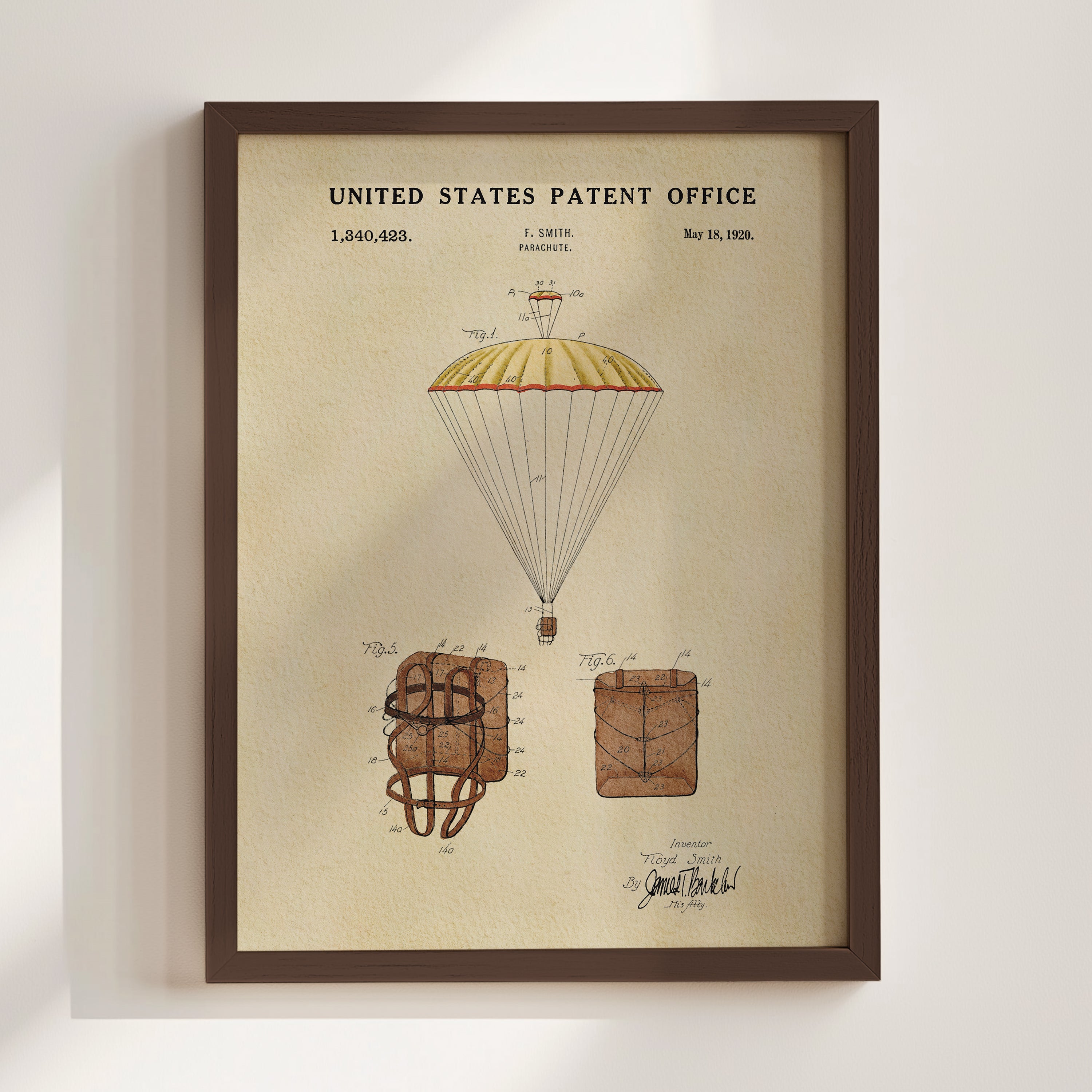 The image is a framed patent drawing depicting a parachute with a yellow and red canopy, along with two smaller parachute models.